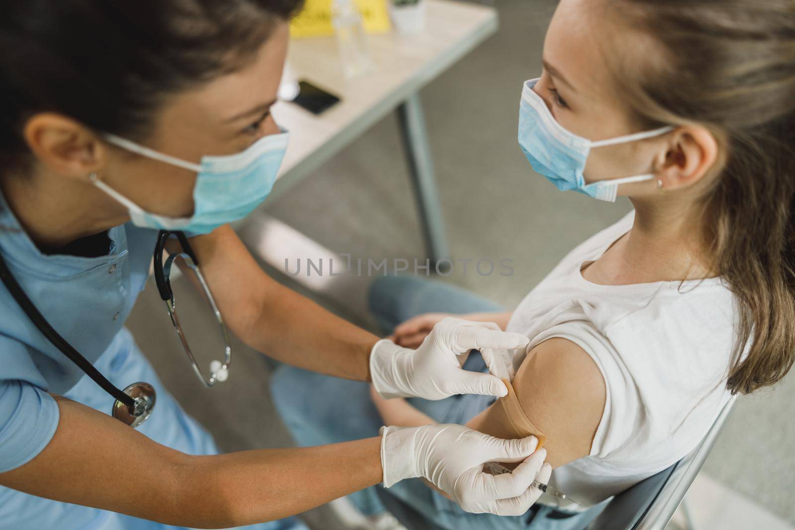 A nurse applying a band aid to a cute teenager girl after receiving the Covid-19 vaccine.