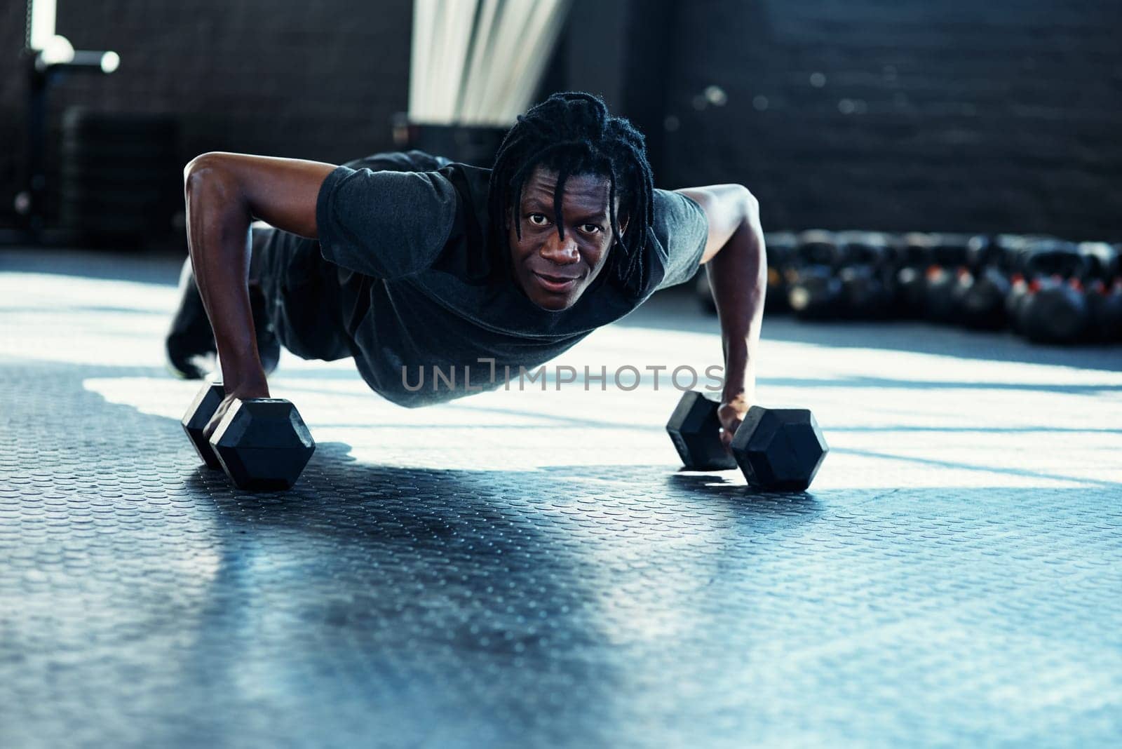 My fitness can only get better if I keep going. a young man doing push ups with dumbbells in a gym
