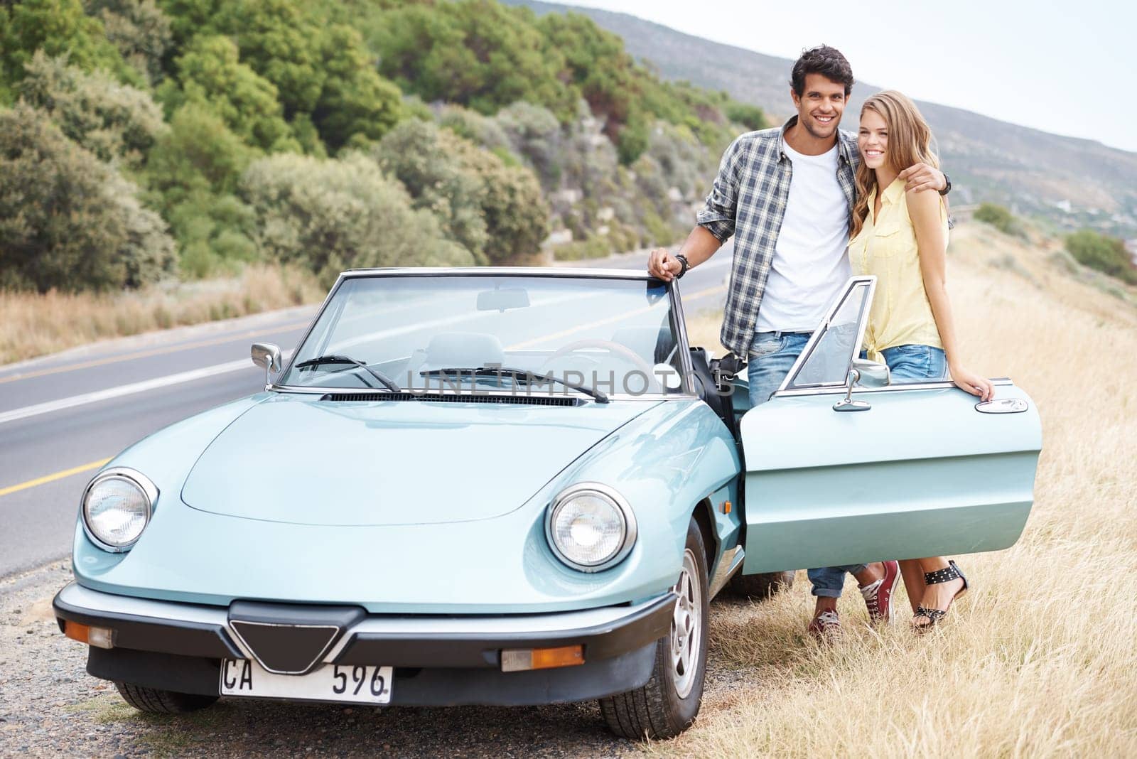 Theyre taking a trip together. A young couple standing alongside their convertible while on a road trip. by YuriArcurs