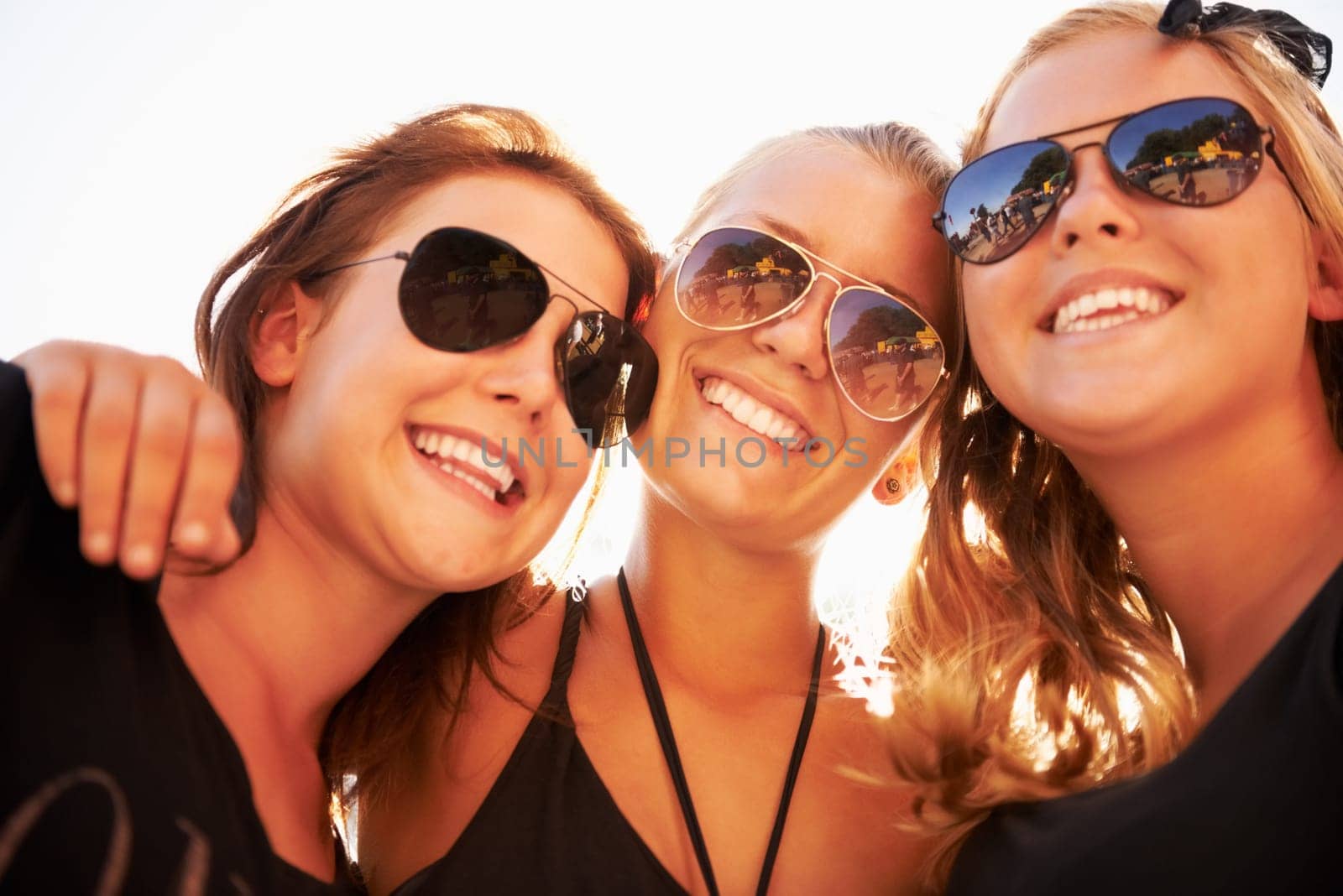 Soaking up the sun. Three friends hugging and smiling against a bright sky