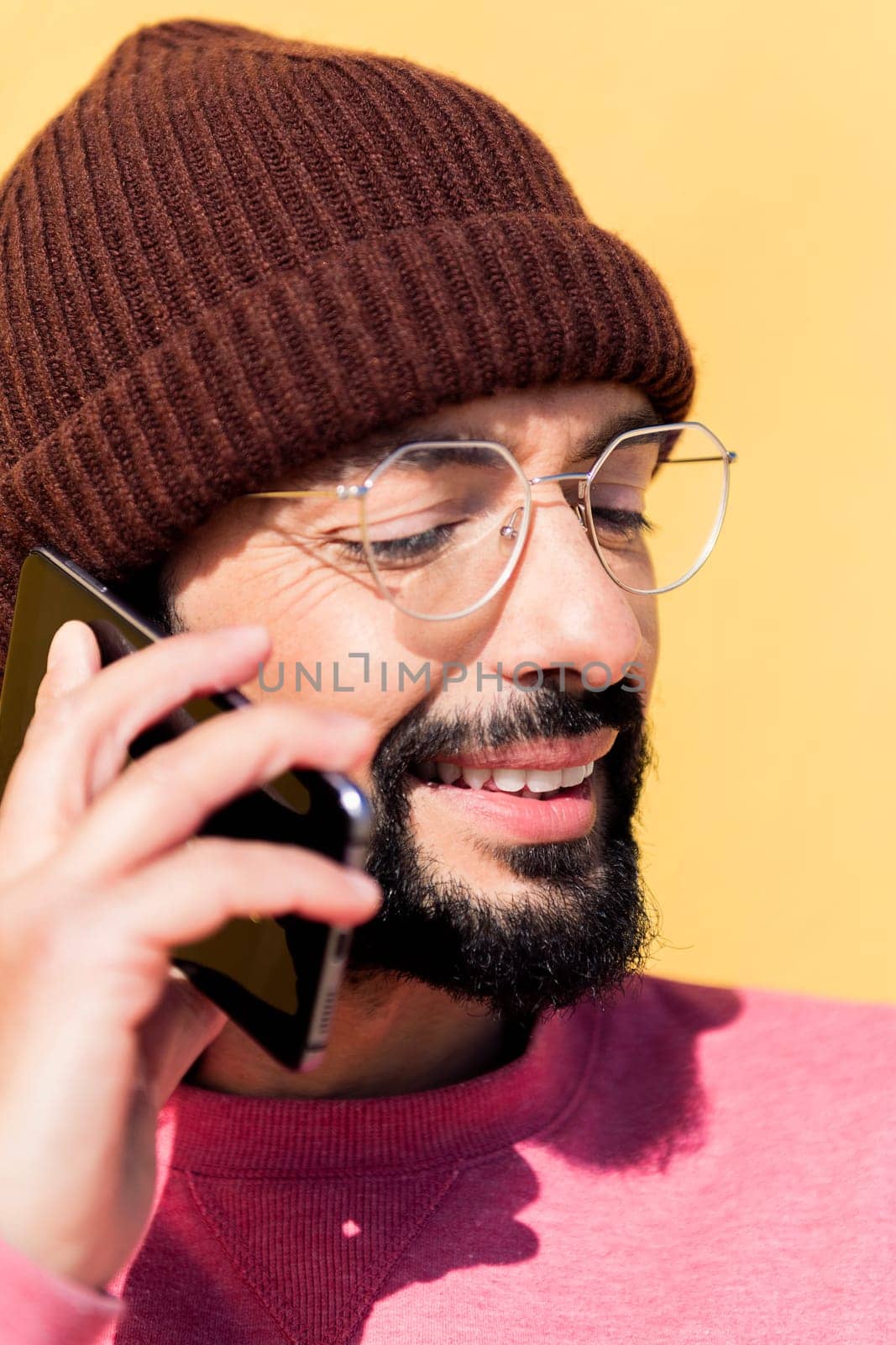 smiling young man talking on mobile phone in a yellow background, concept of technology of communication and modern lifestyle