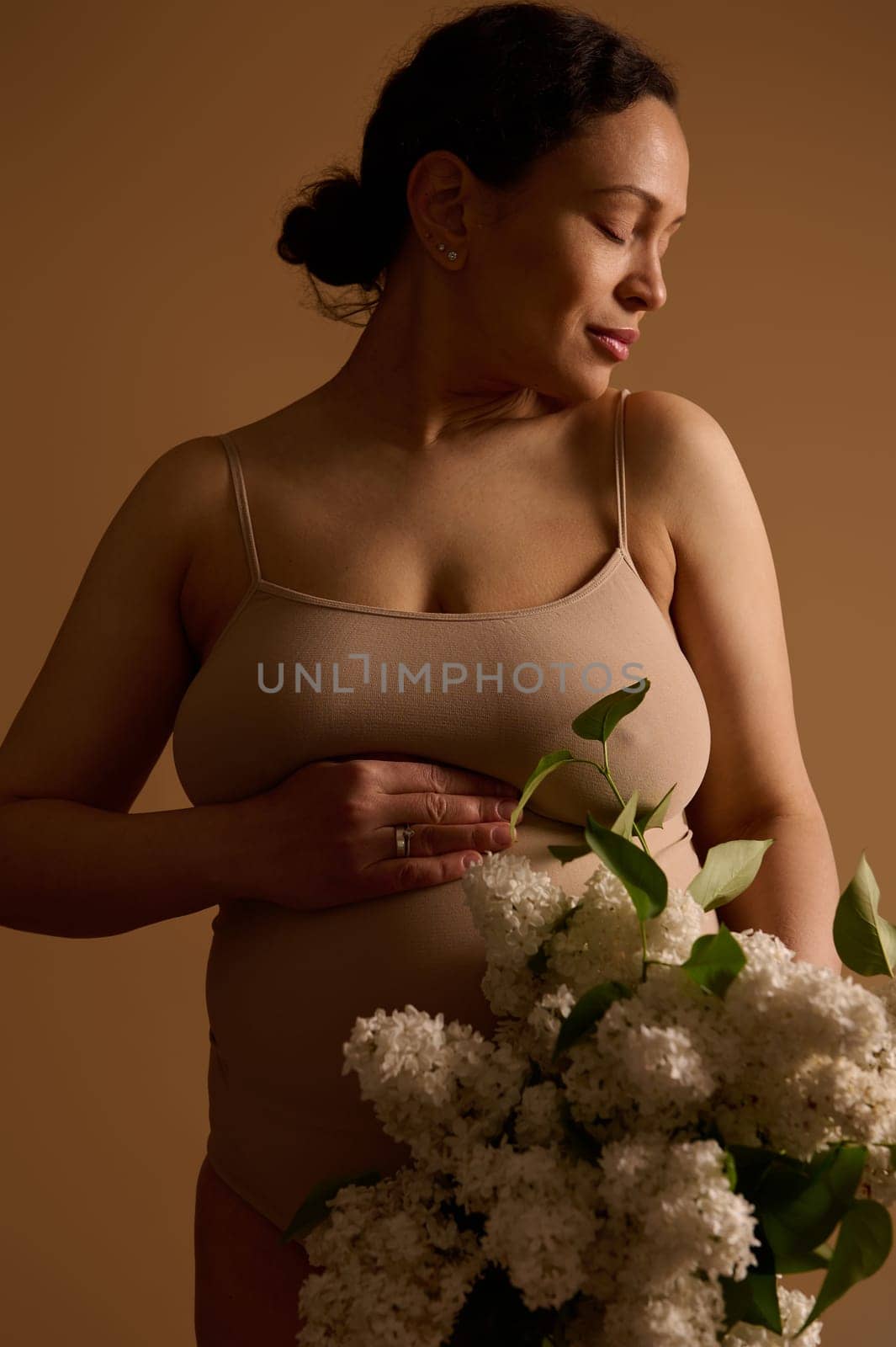 Pregnancy. Maternity. Expecting a baby. Delightful pregnant woman in beige lingerie with blooming white lilacs by artgf