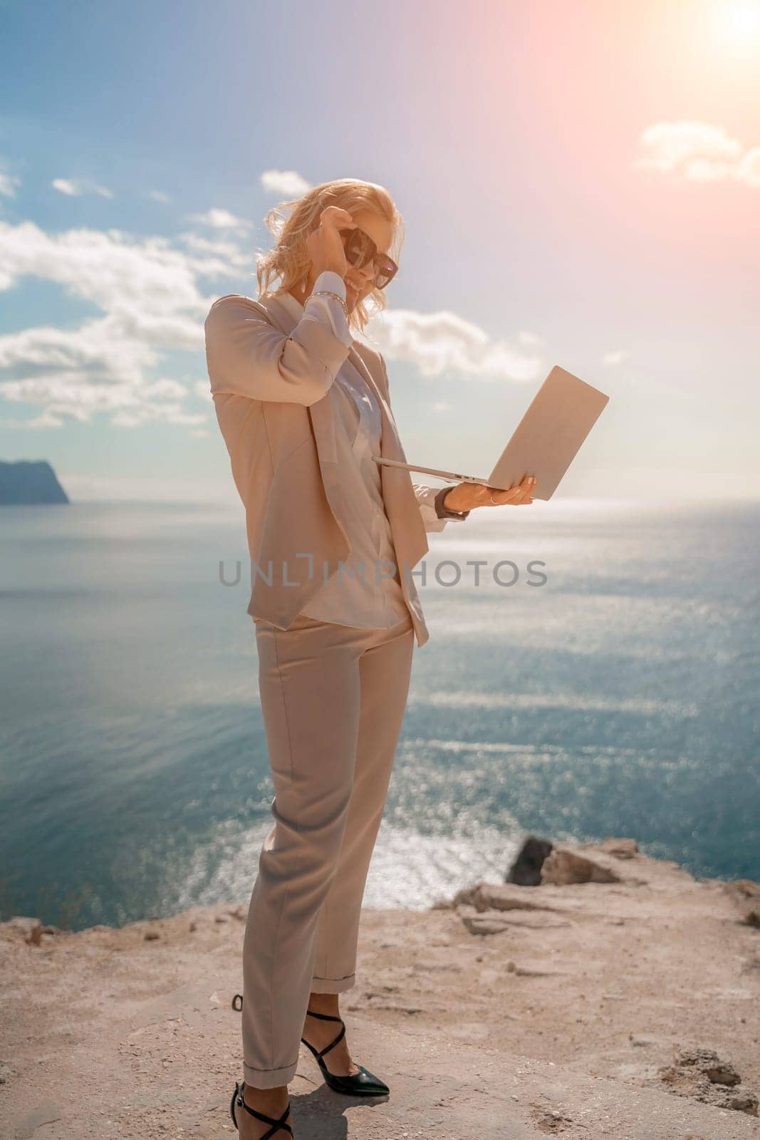 Freelance women sea. She is working on the computer. Good looking middle aged woman typing on a laptop keyboard outdoors with a beautiful sea view. The concept of remote work