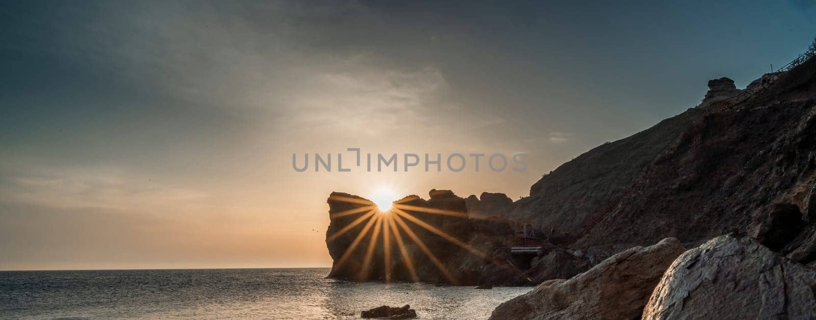 Banner. In blur An epic sunset on the sea - the sun sets behind the mountain and everything shines with warm light with long rays. by Matiunina