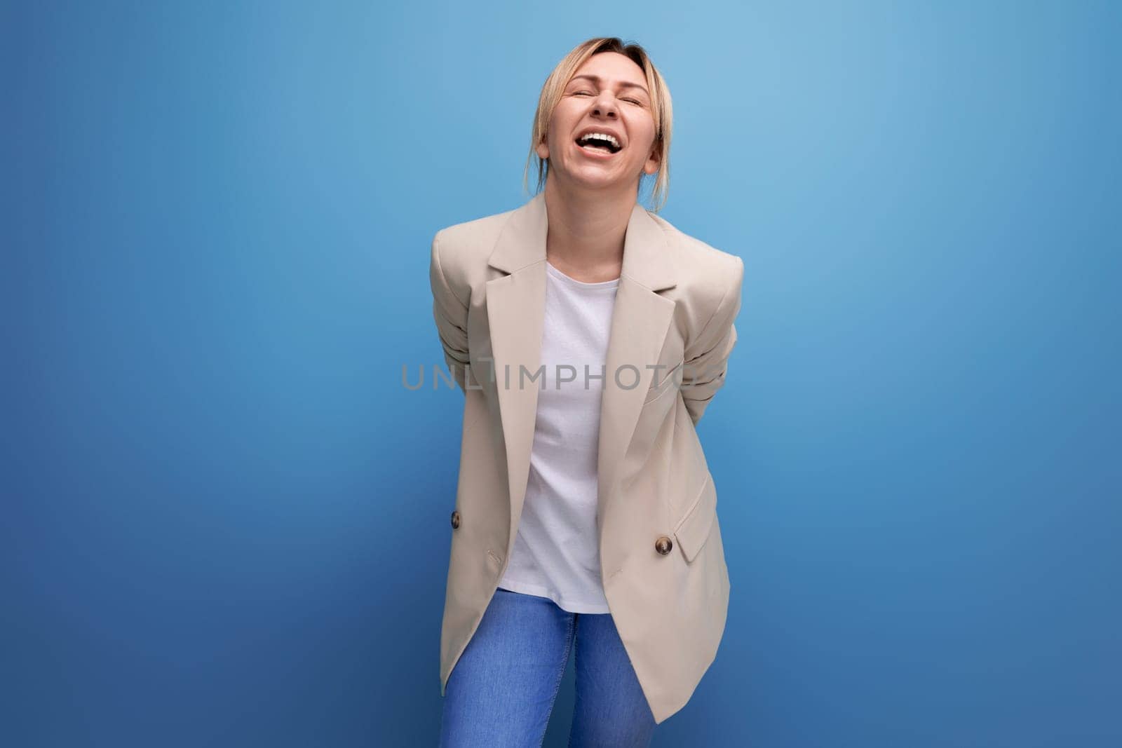 laughing blonde young business woman in jacket on studio background.