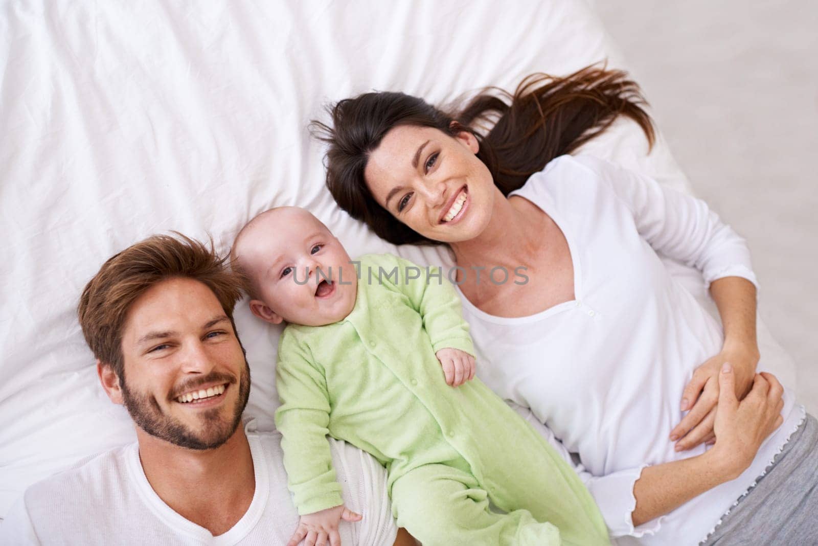 Top view, portrait and happy parents with baby on bed for love, care and quality time together at home. Smile of mother, father and family with cute newborn kid relaxing in bedroom, fun and happiness.