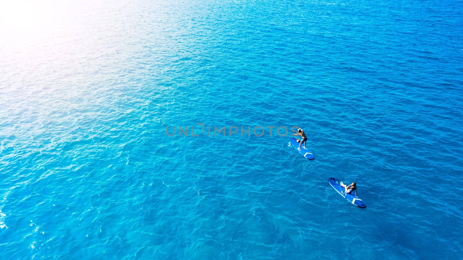 As blue as blue gets. a man and woman paddle boarding across the sea. by YuriArcurs