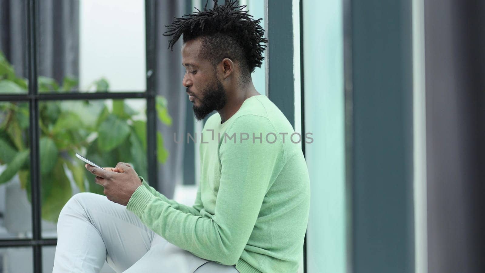 African American man talking on the phone while sitting in an office corridor by Prosto