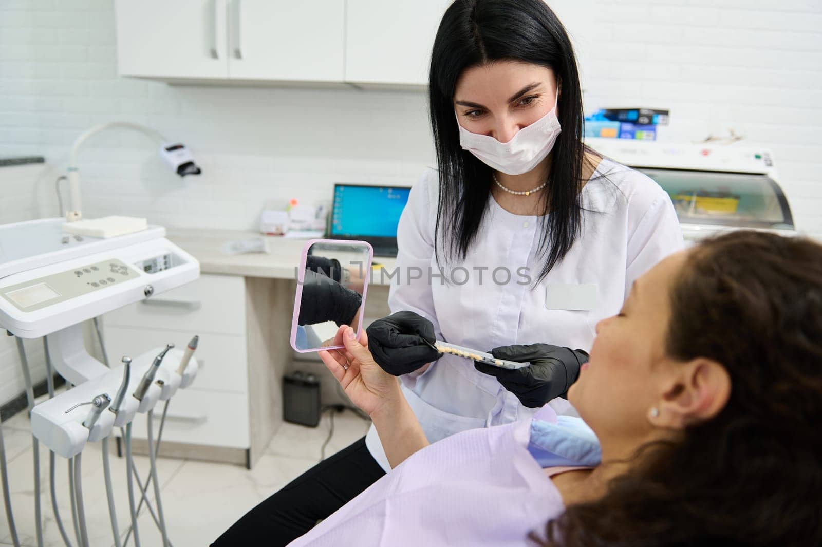 Dentist doctor holding teeth color chart, discussing with patient the teeth prosthesis and bleaching in dentistry clinic by artgf