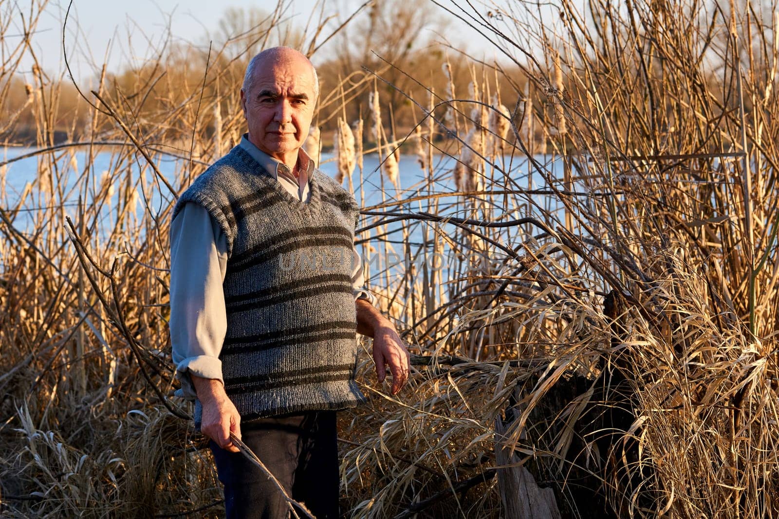 Elderly cheerful pensioner in a picnic in nature among the reeds on the lake by jovani68