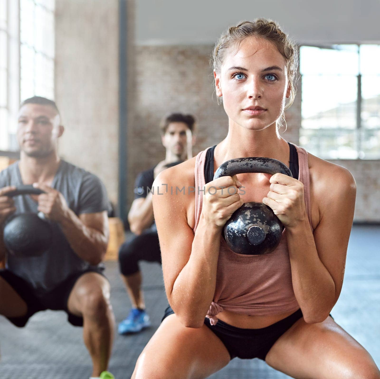 Sports, kettlebell and woman doing a workout with a group for strength training in a gym. Fitness, energy and female athlete doing a exercise challenge with weights with people in a wellness center. by YuriArcurs