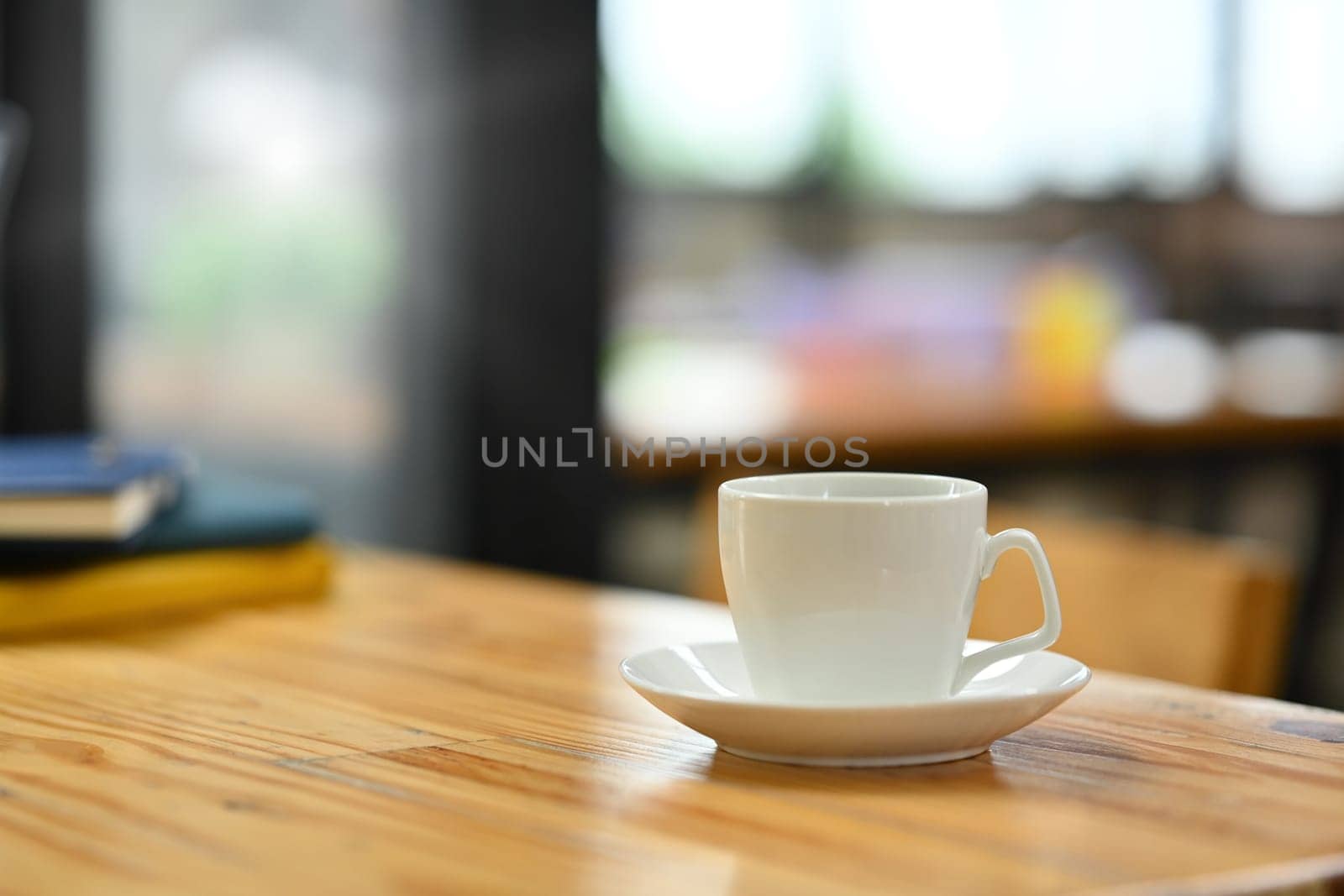 Closeup white cup of coffee and books on wooden office desk. Empty area left side of image for your text by prathanchorruangsak