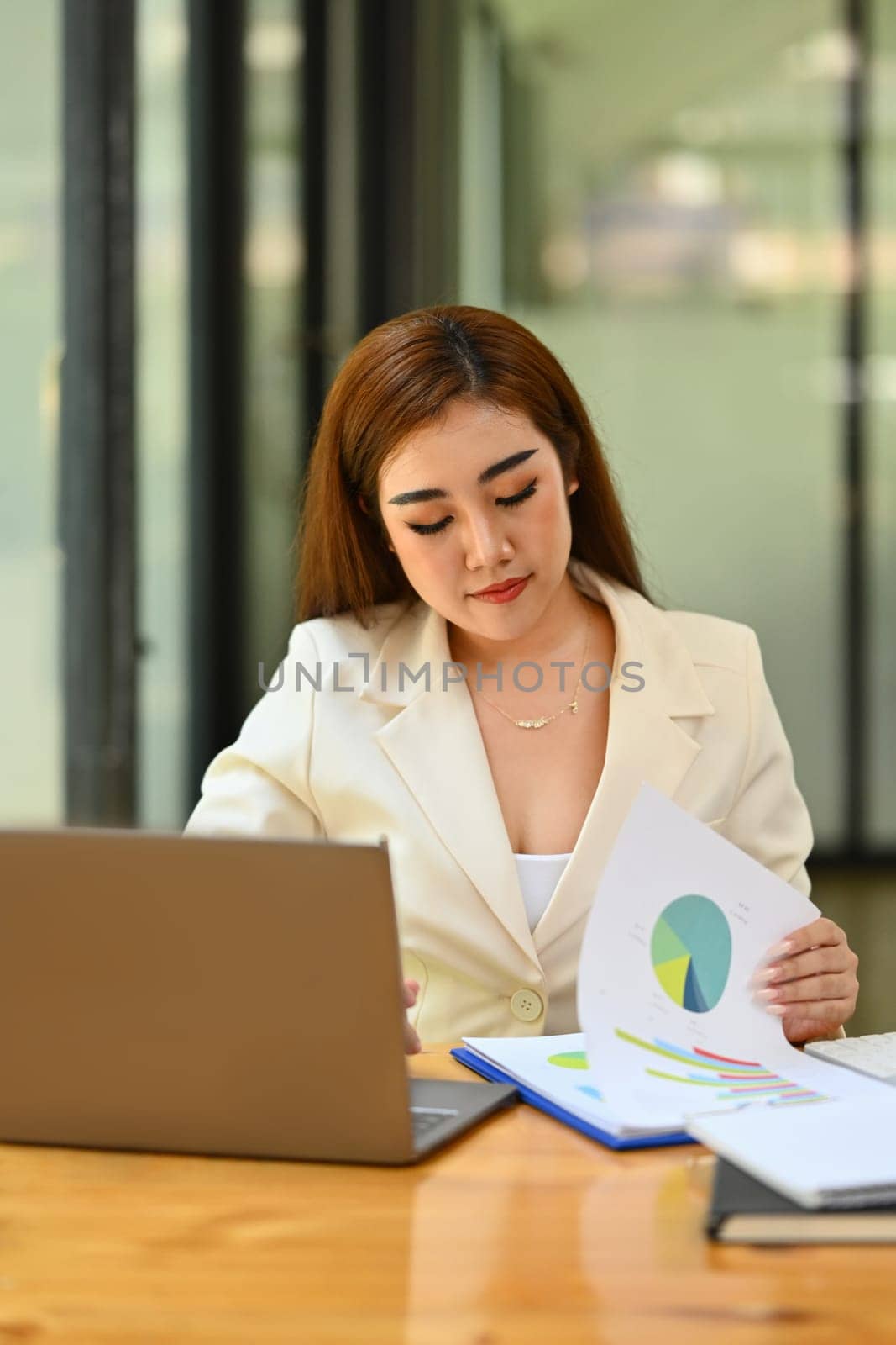 Focused female economist sitting at desk with laptop, reviewing marketing research results or statistics data.