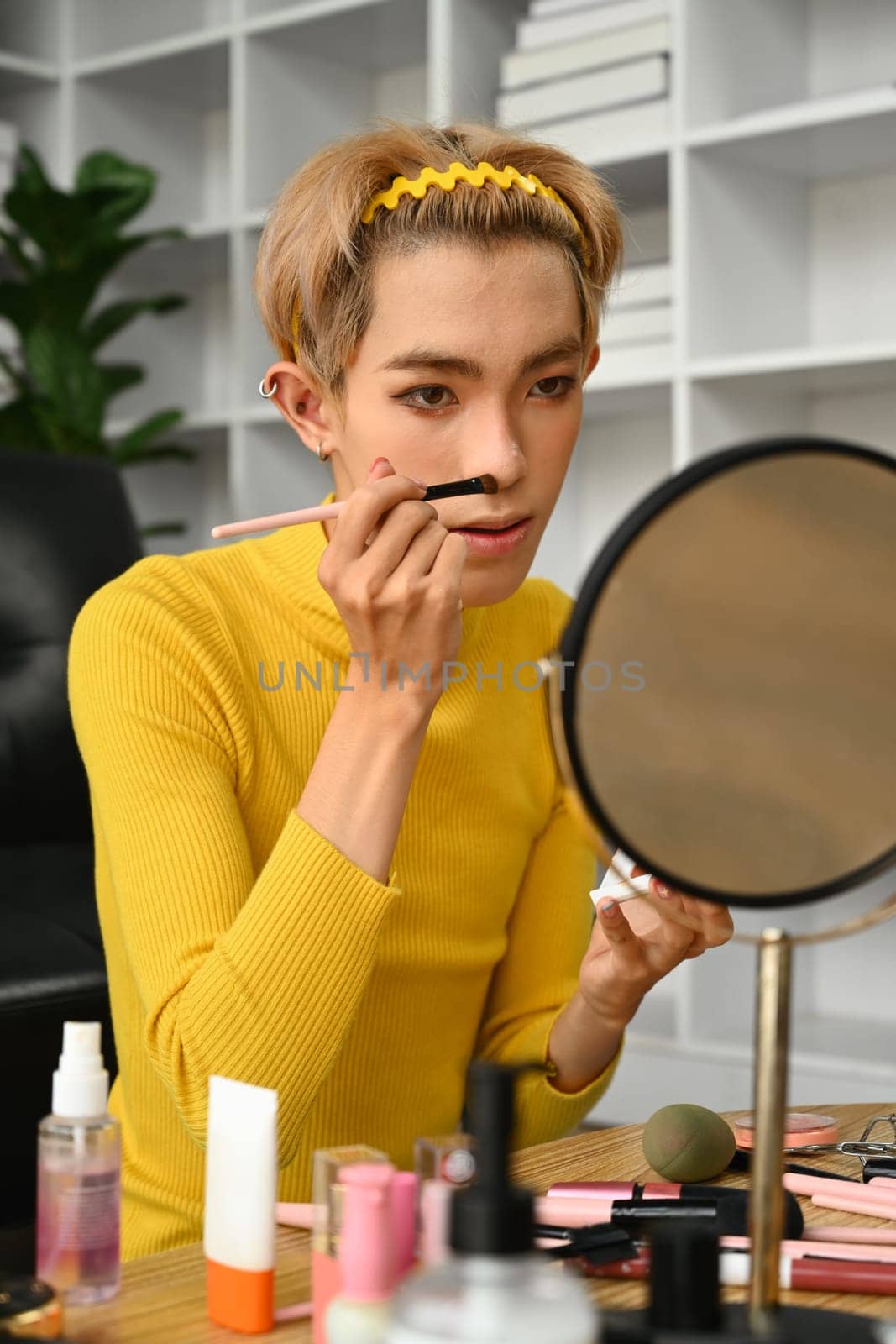 Charming young gay man blogger recording make up tutorial, live streaming at home. LGBTQ lifestyle, influencer, blogger.