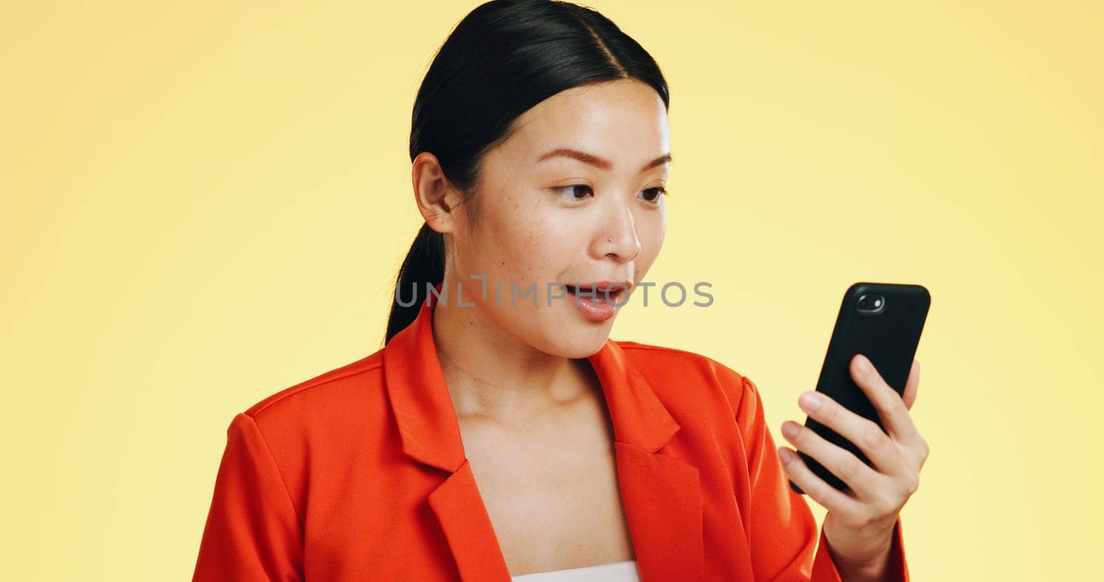 Winner, success celebration and Asian woman with phone in studio isolated on a yellow background. Surprise, fist pump or happy female with mobile to celebrate after winning lottery prize or good news.