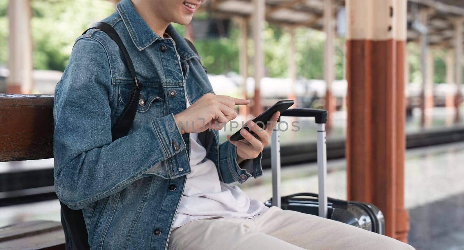 Young handsome man sitting and using smartphone at train station.