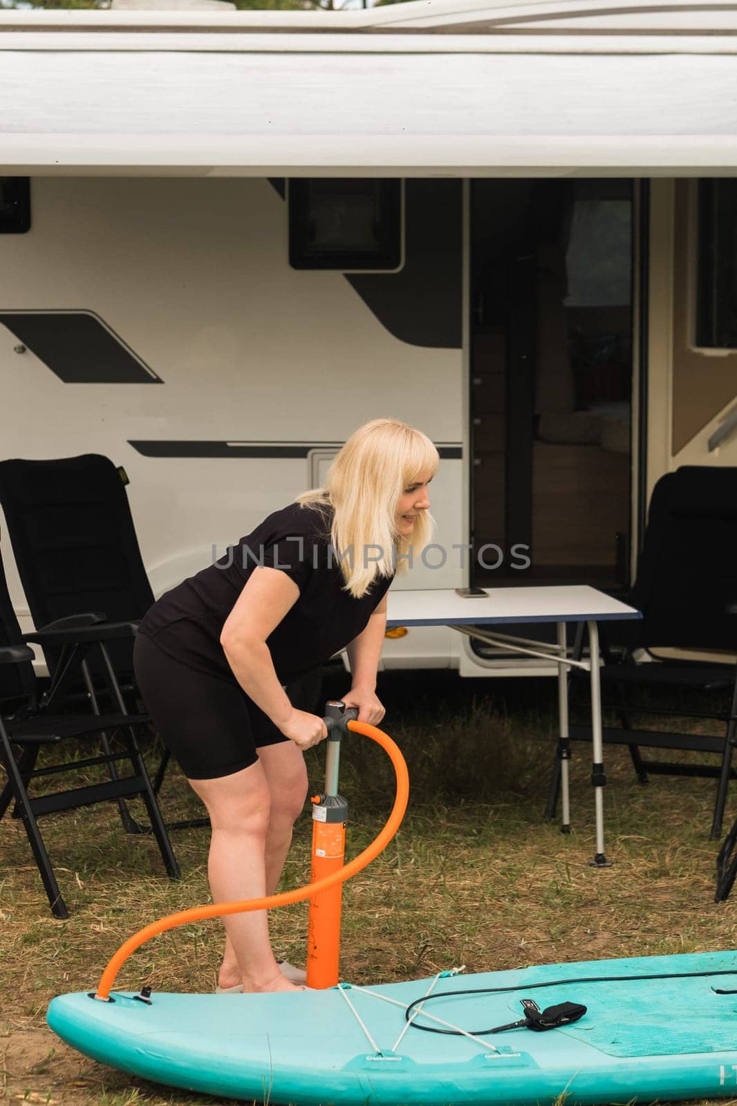 A woman inflates a sup-board for swimming near her motorhome by Lobachad