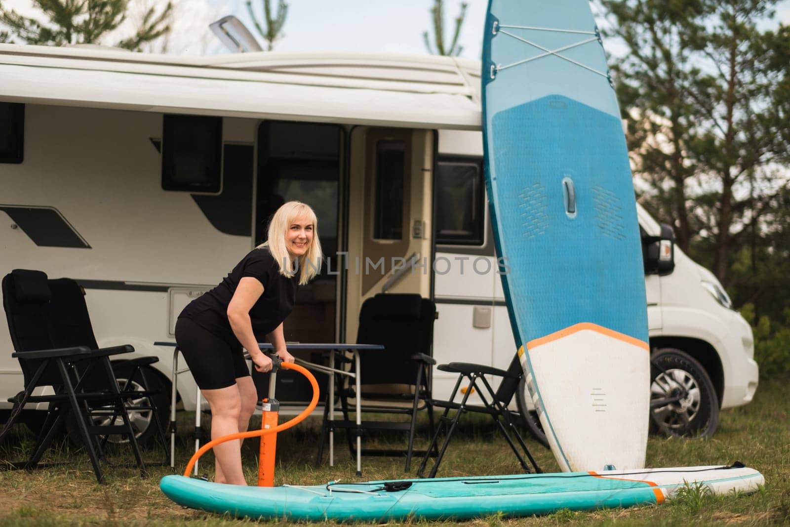 A woman inflates a sup-board for swimming near her motorhome.