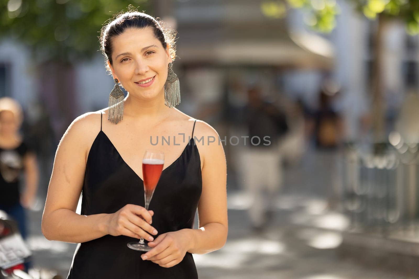 Smiling woman at casual party in elegant dress holding a drink. Mid shot