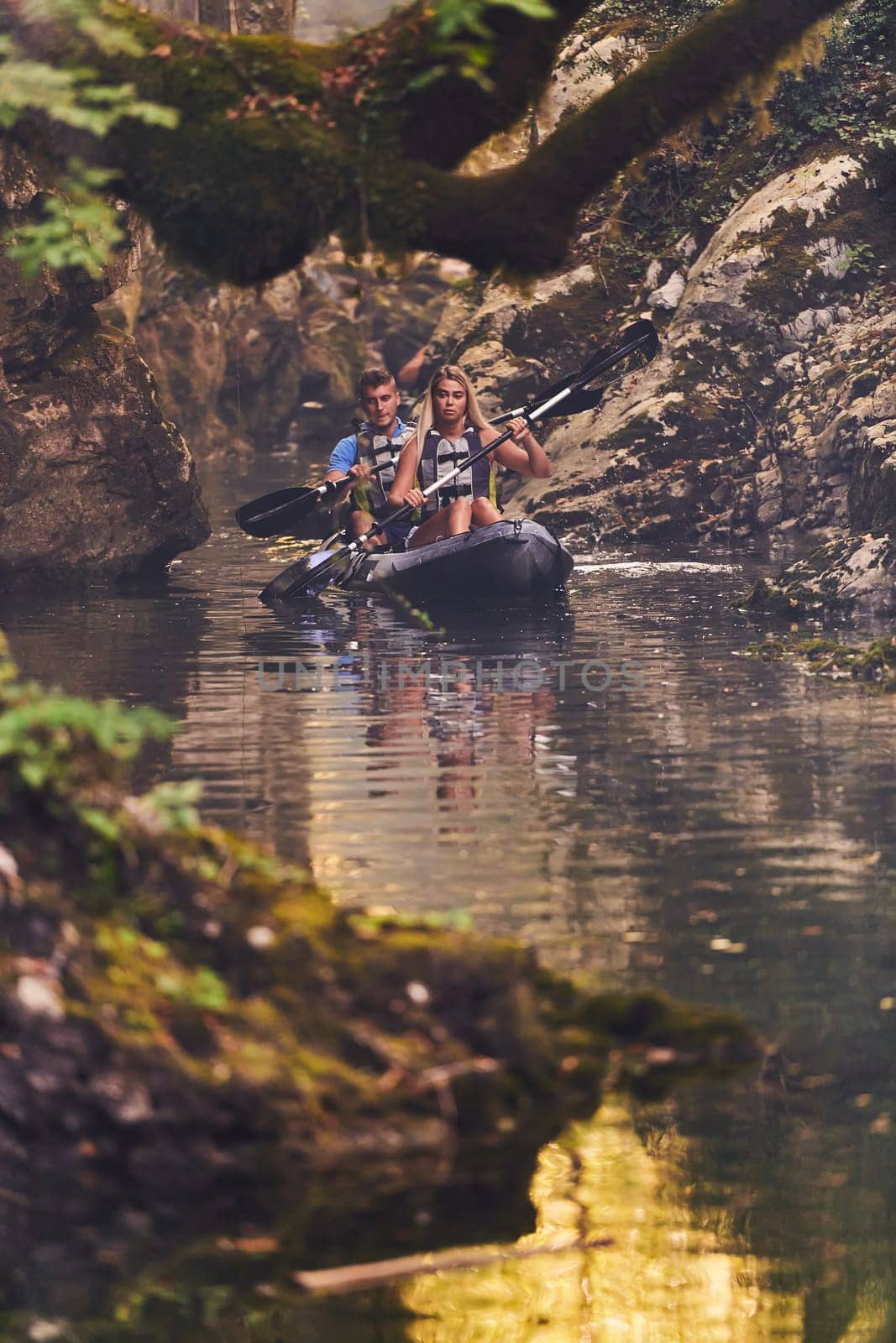 A young couple enjoying an idyllic kayak ride in the middle of a beautiful river surrounded by forest greenery.