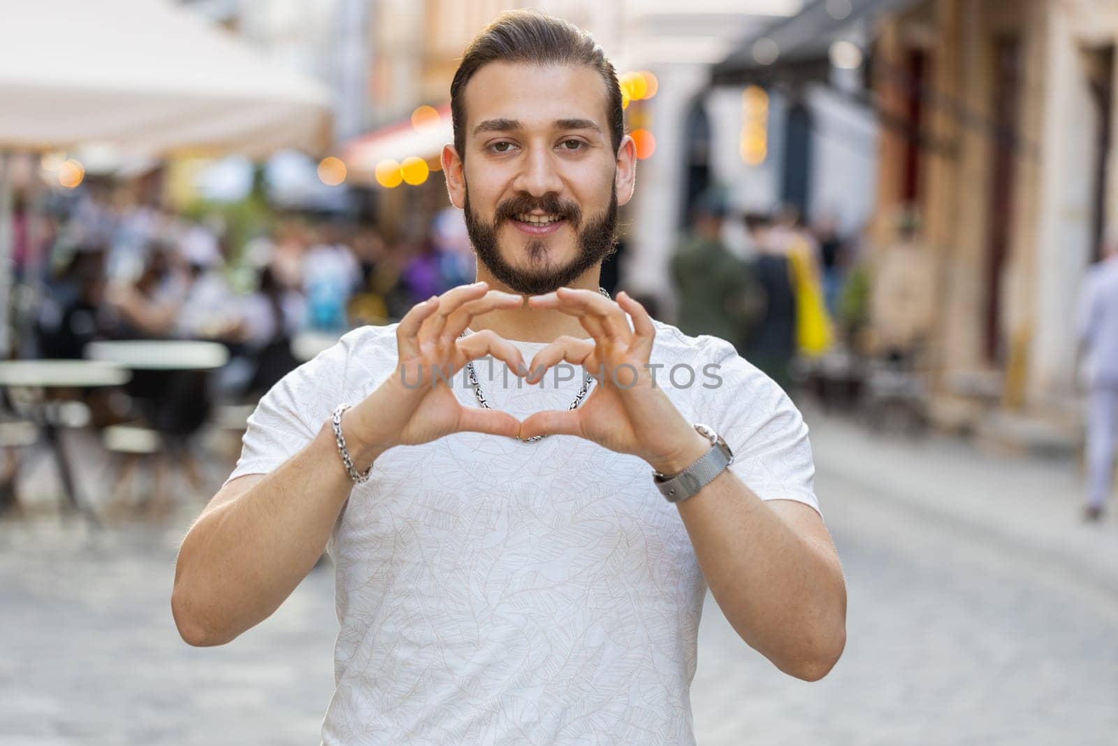 I love you. Young man makes symbol of love, showing heart sign to camera, express romantic feelings, express sincere positive feelings. Charity, gratitude, donation. Outdoors in urban city street