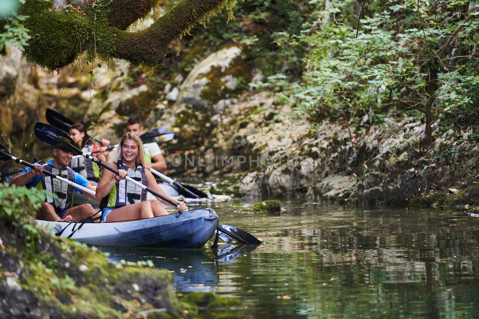 A group of friends enjoying having fun and kayaking while exploring the calm river, surrounding forest and large natural river canyons by dotshock