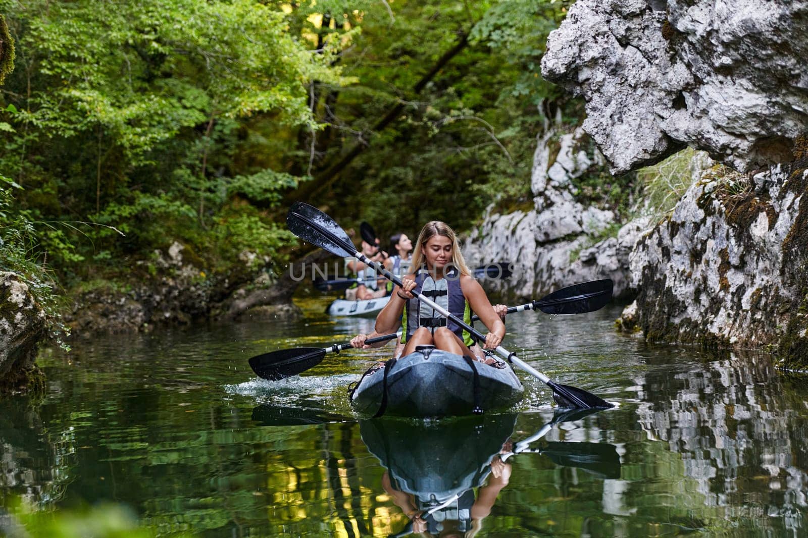 A group of friends enjoying having fun and kayaking while exploring the calm river, surrounding forest and large natural river canyons by dotshock