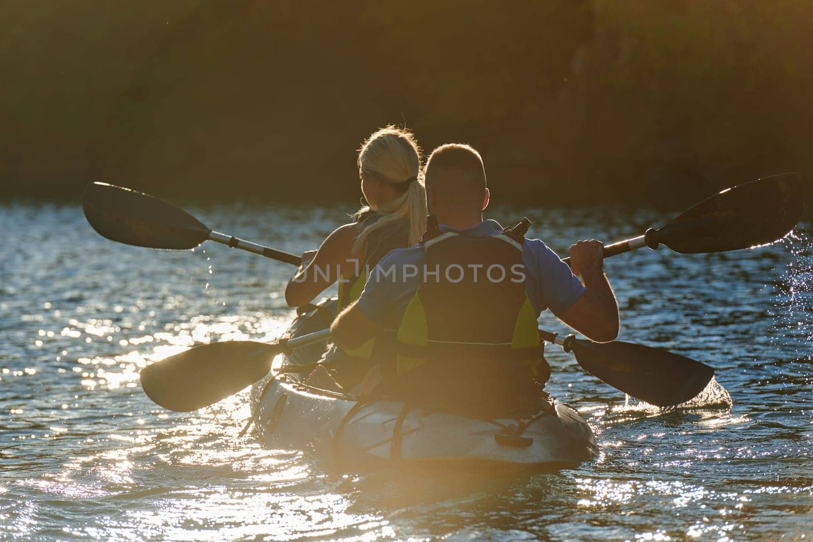 A young couple enjoying an idyllic kayak ride in the middle of a beautiful river surrounded by forest greenery in sunset time by dotshock