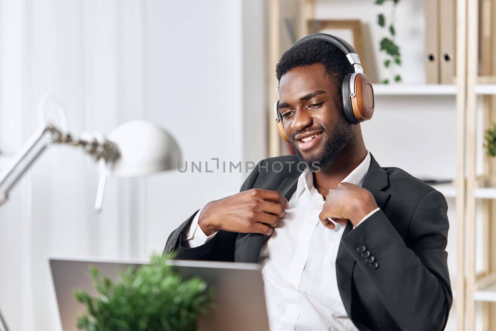 An African-American man sits at his desk in front of his laptop, wearing headphones and chatting on a video call, listening to music. The concept of student business training and online work. High quality photo