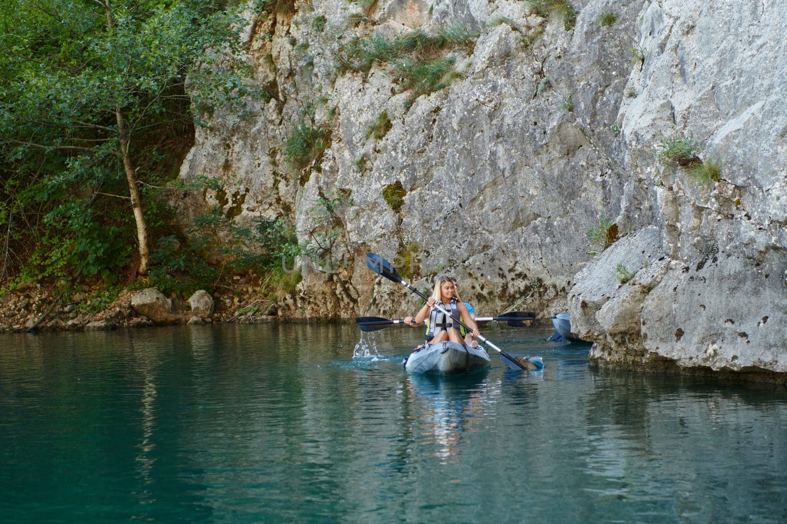 A group of friends enjoying having fun and kayaking while exploring the calm river, surrounding forest and large natural river canyons.