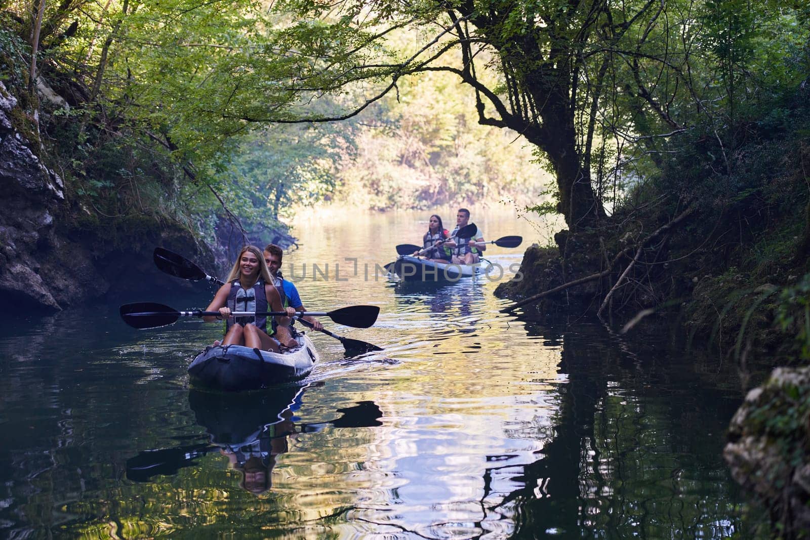 A group of friends enjoying having fun and kayaking while exploring the calm river, surrounding forest and large natural river canyons by dotshock