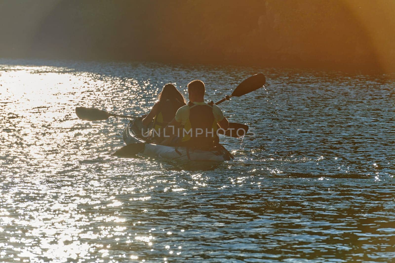 A young couple enjoying an idyllic kayak ride in the middle of a beautiful river surrounded by forest greenery in sunset time.