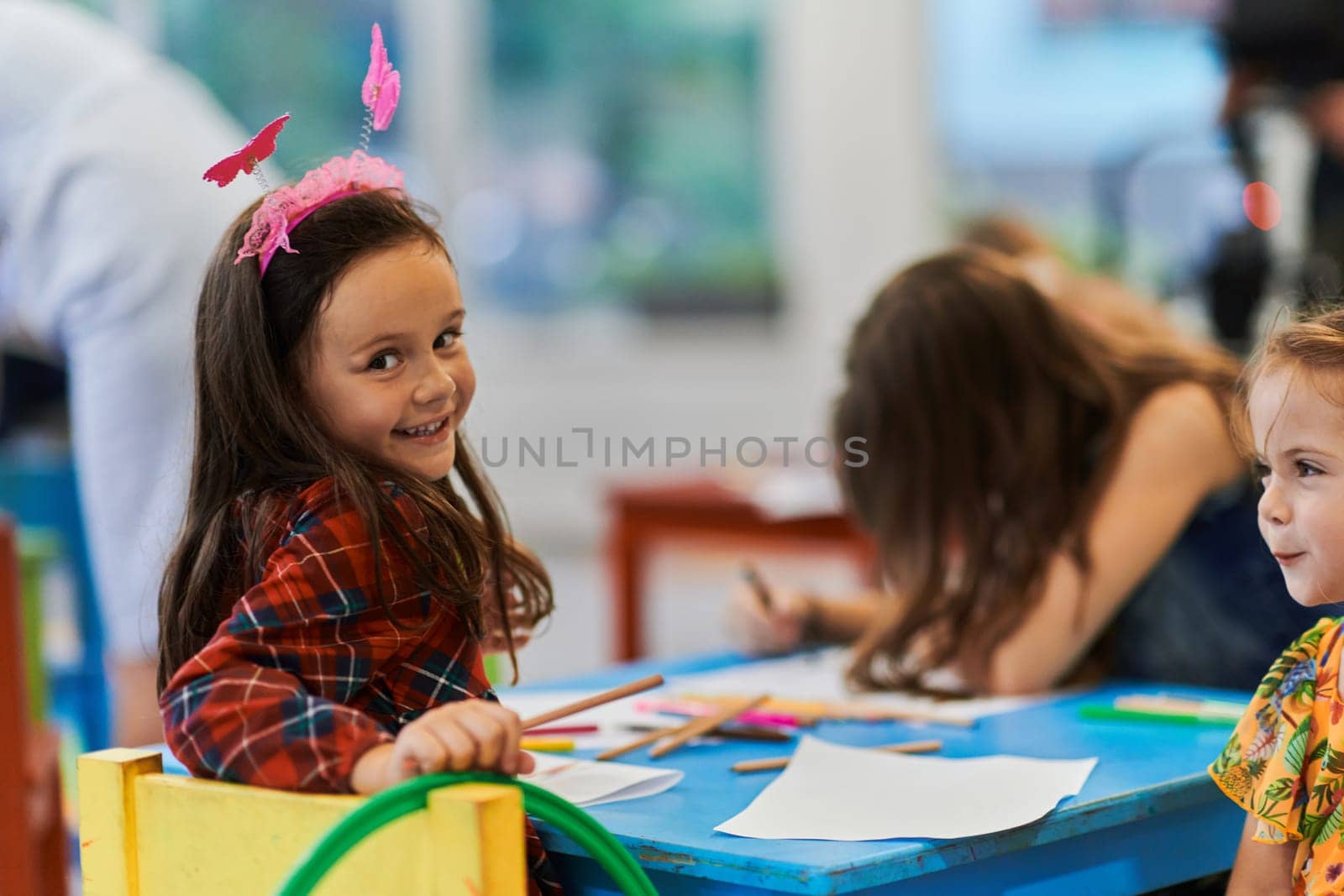 Creative kids during an art class in a daycare center or elementary school classroom drawing with female teacher