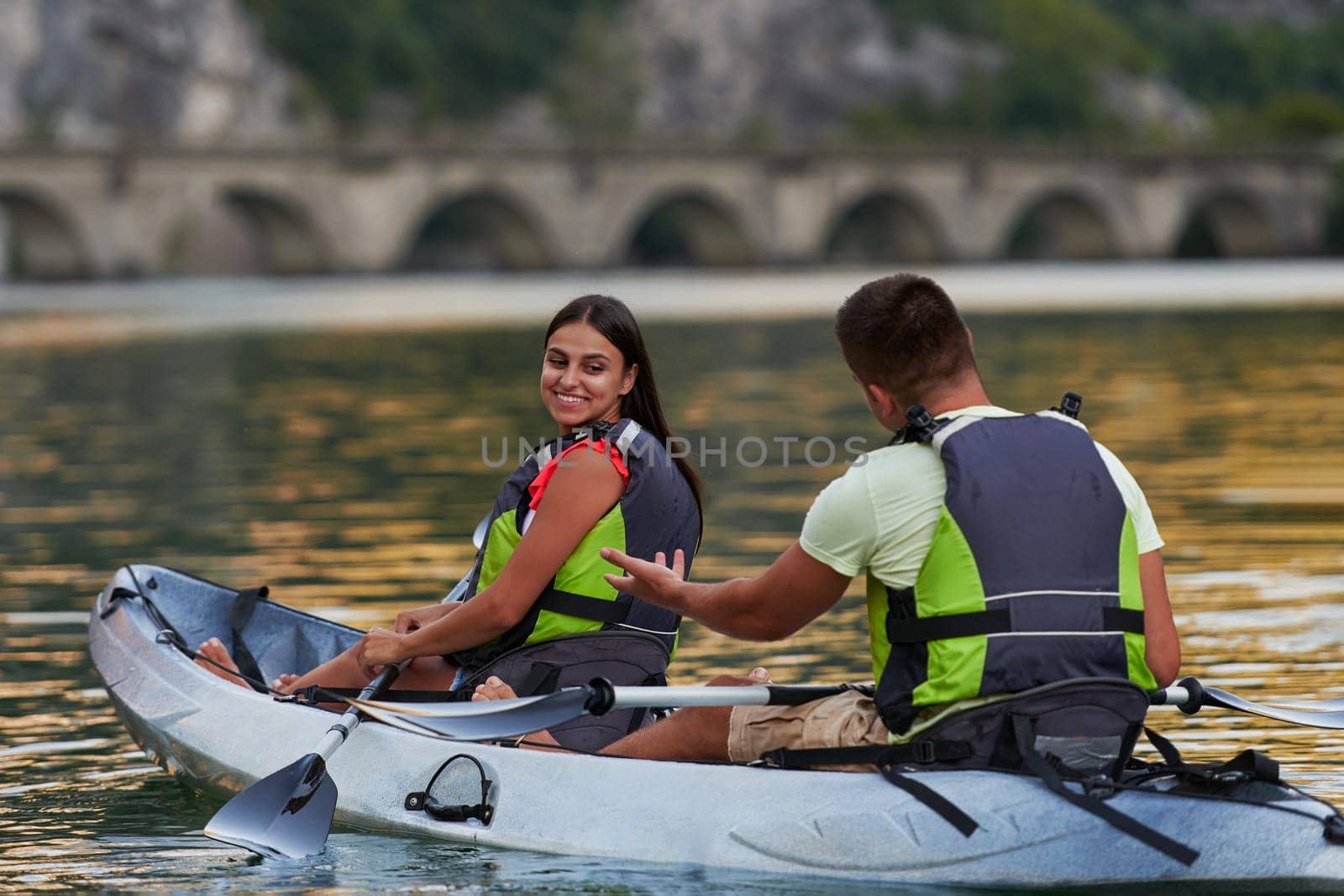 A young couple enjoying an idyllic kayak ride in the middle of a beautiful river surrounded by forest greenery by dotshock