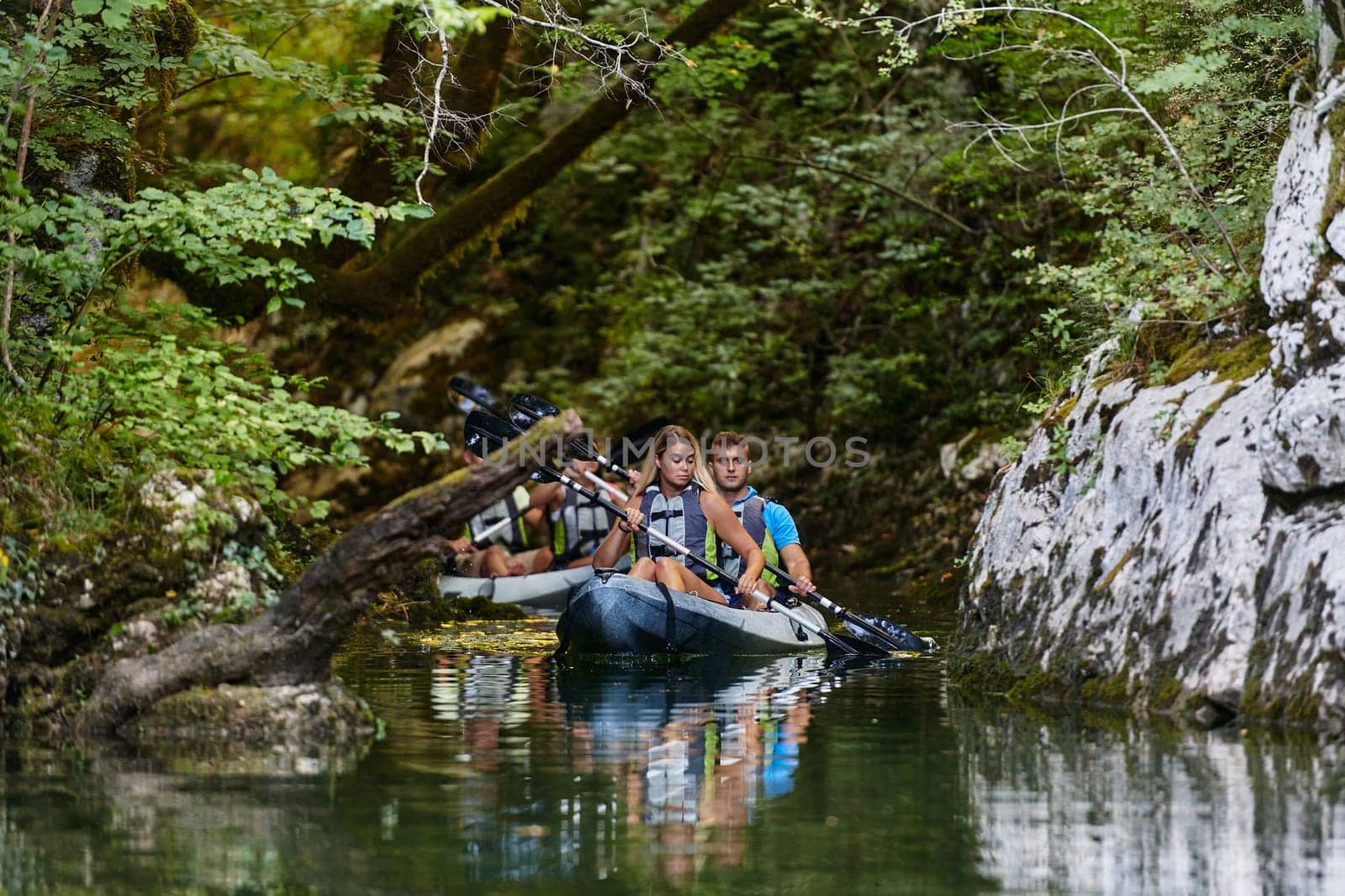 A group of friends enjoying having fun and kayaking while exploring the calm river, surrounding forest and large natural river canyons by dotshock