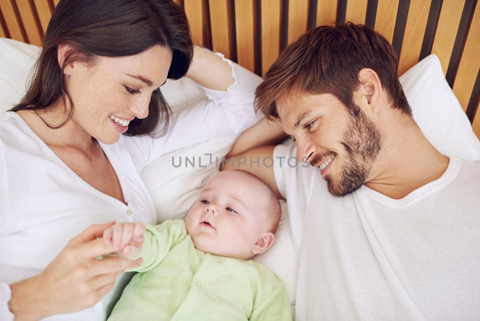 Top view, parents and smile of baby in bedroom for love, care and quality time together at home. Happy mother, father and family relax with cute newborn kid on bed for support, development and joy.
