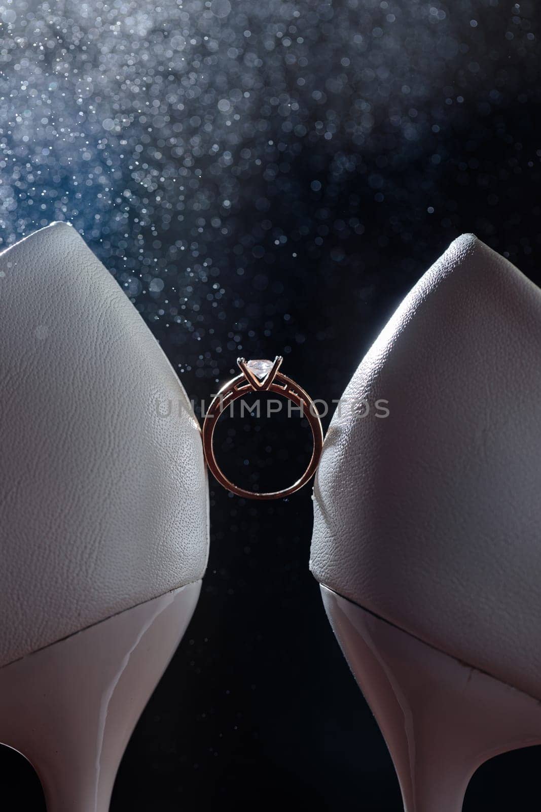Gold ring of the bride with a pebble between white shoes with heels. Bride's precious ring