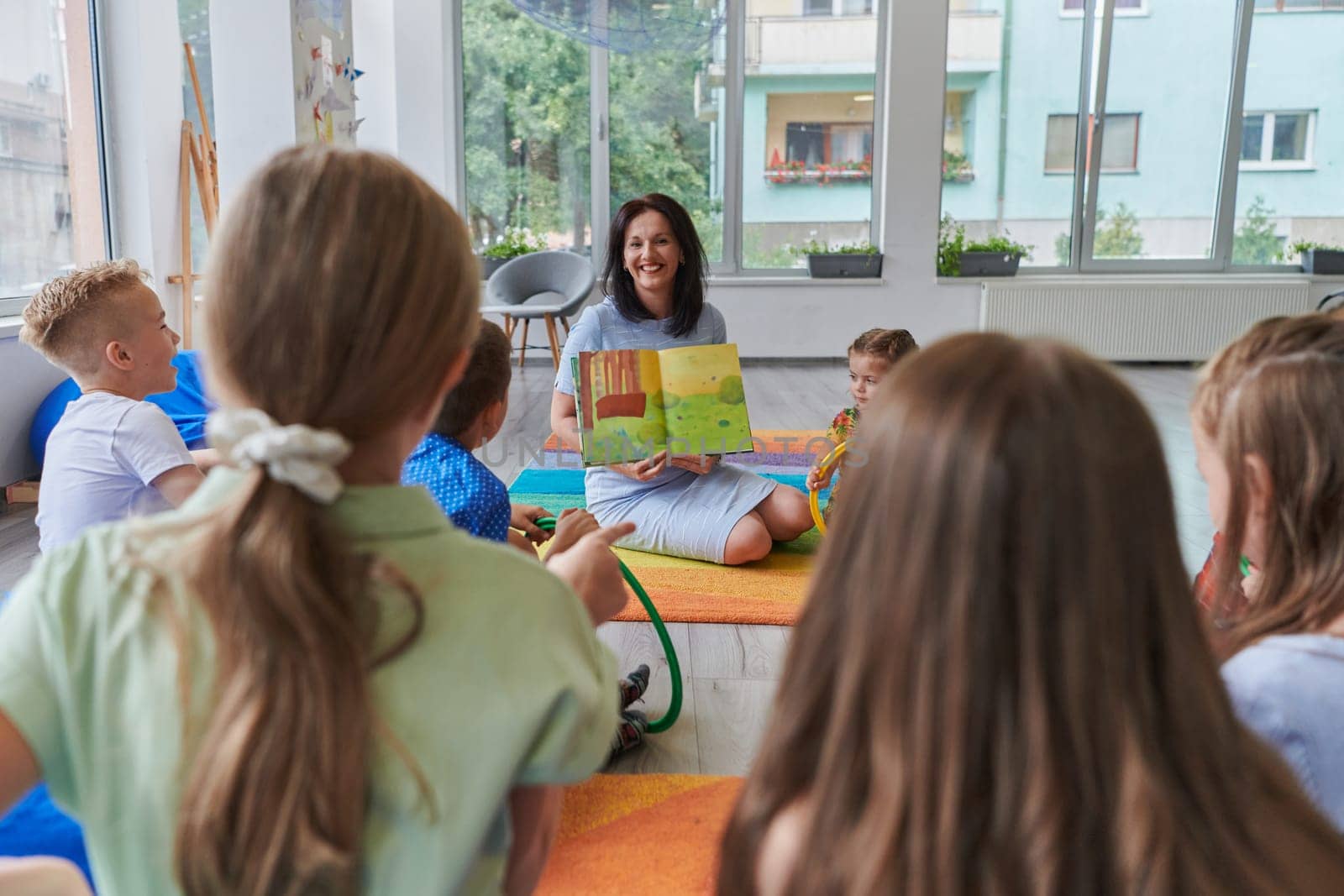 Reading time in an elementary school or kindergarten, a teacher reading a book to children in an elementary school or kindergarten. The concept of pre-school education. Selective focus by dotshock