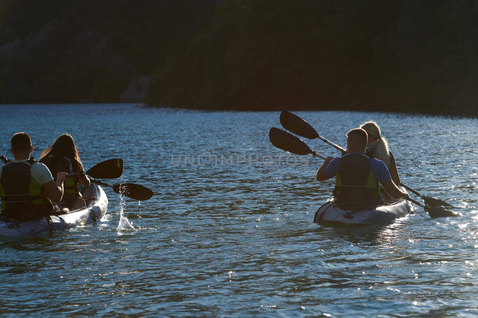 A group of friends enjoying fun and kayaking exploring the calm river, surrounding forest and large natural river canyons during an idyllic sunset