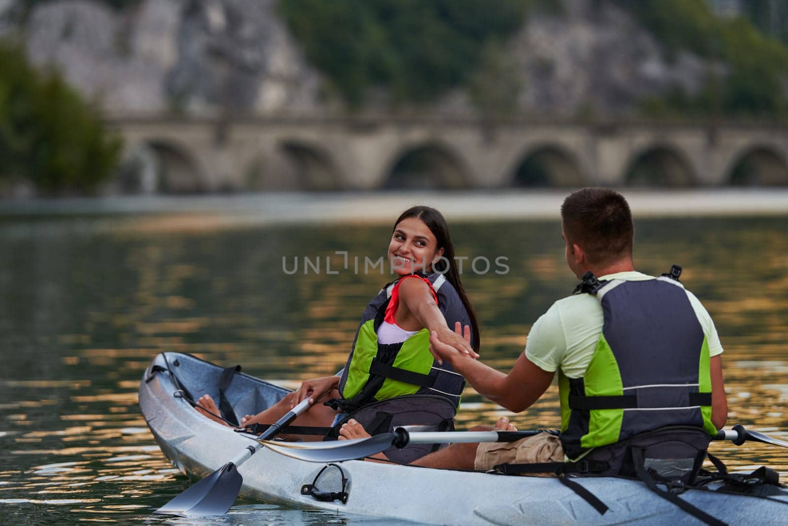 A young couple enjoying an idyllic kayak ride in the middle of a beautiful river surrounded by forest greenery.