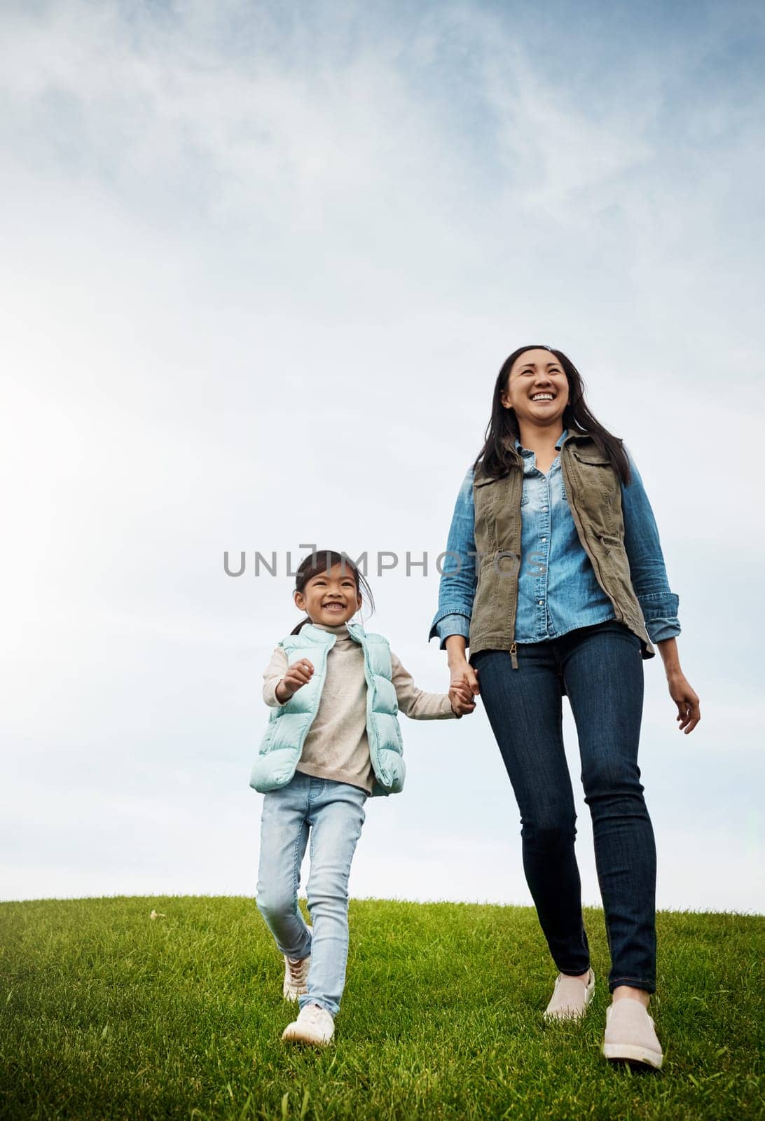 Its all smiles when were outside. a woman holding her little girls hand as they walk outdoors. by YuriArcurs