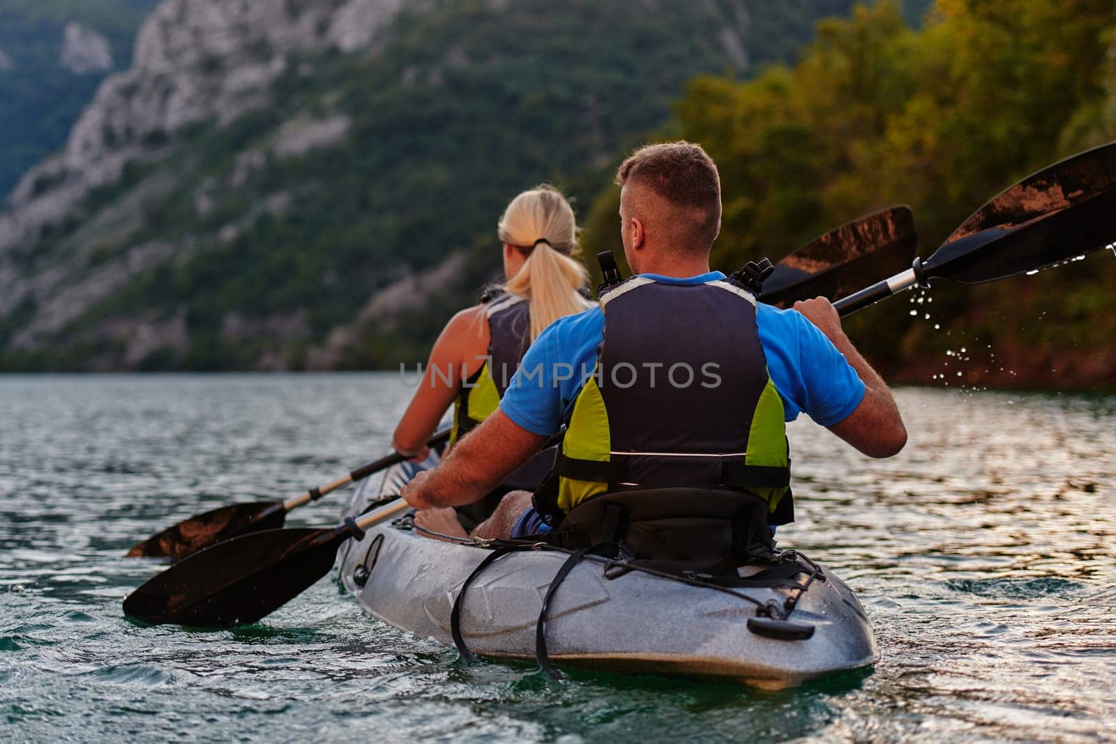 A young couple enjoying an idyllic kayak ride in the middle of a beautiful river surrounded by forest greenery in sunset time.