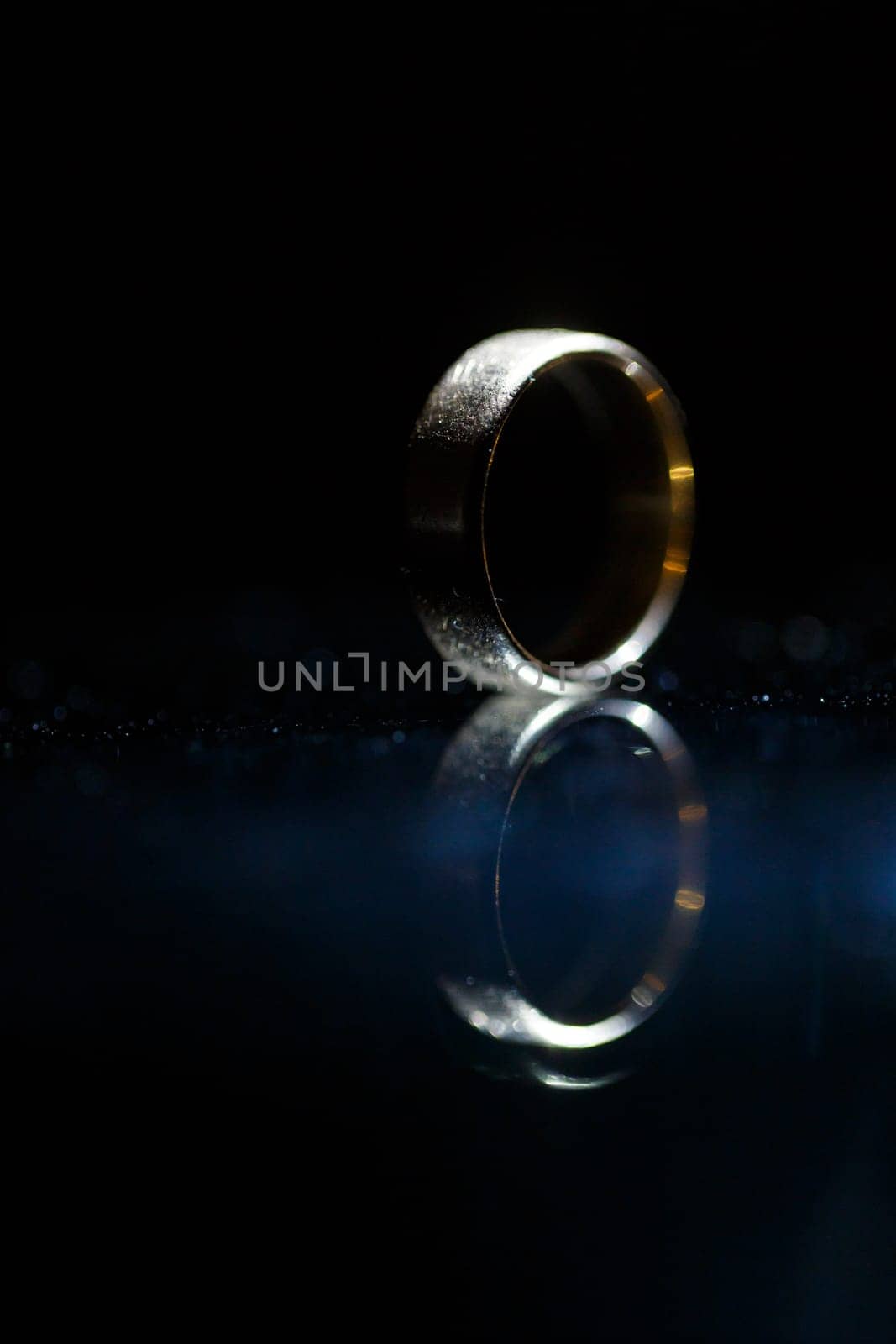 Gold wedding ring on black glass by Dmitrytph