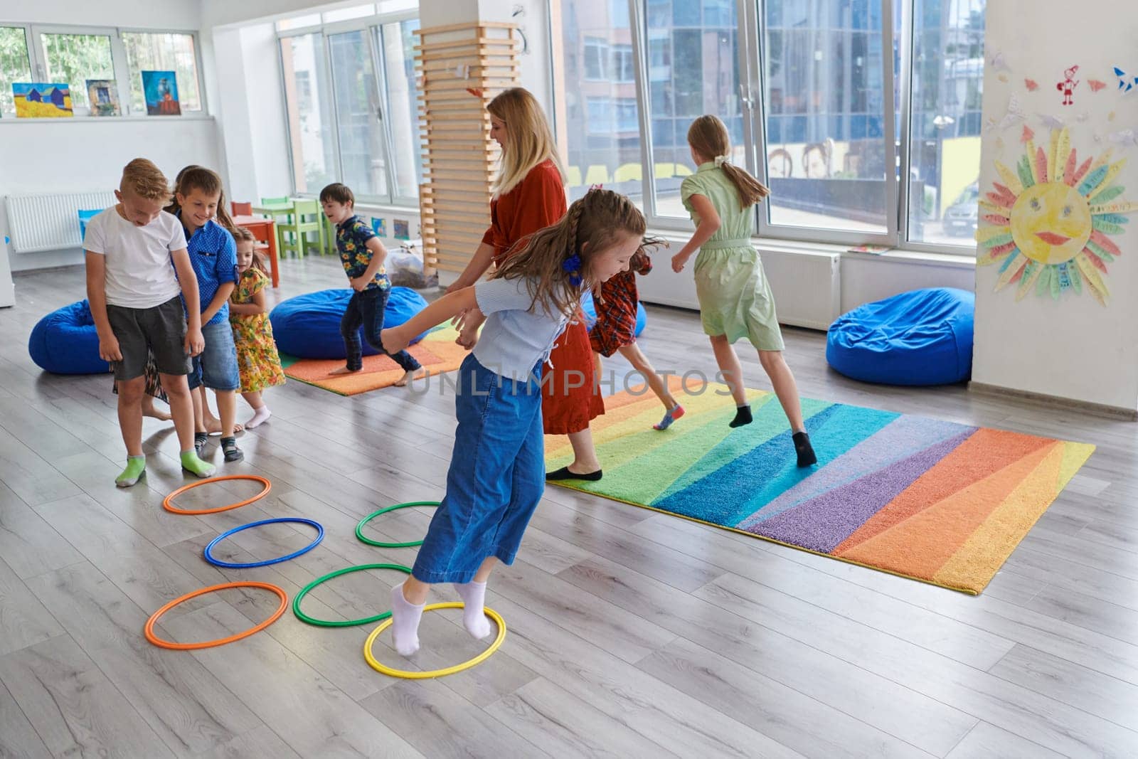 Small nursery school children with female teacher on floor indoors in classroom, doing exercise. Jumping over hula hoop circles track on the floor. by dotshock