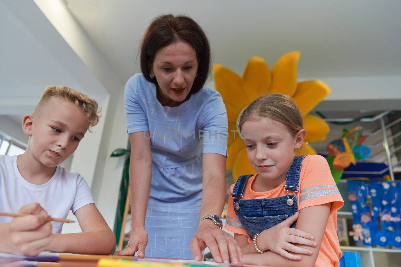 Creative kids during an art class in a daycare center or elementary school classroom drawing with female teacher