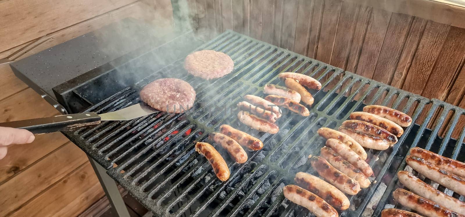 Fresh sausage and hot dogs grilling outdoors on a gas barbecue grill.