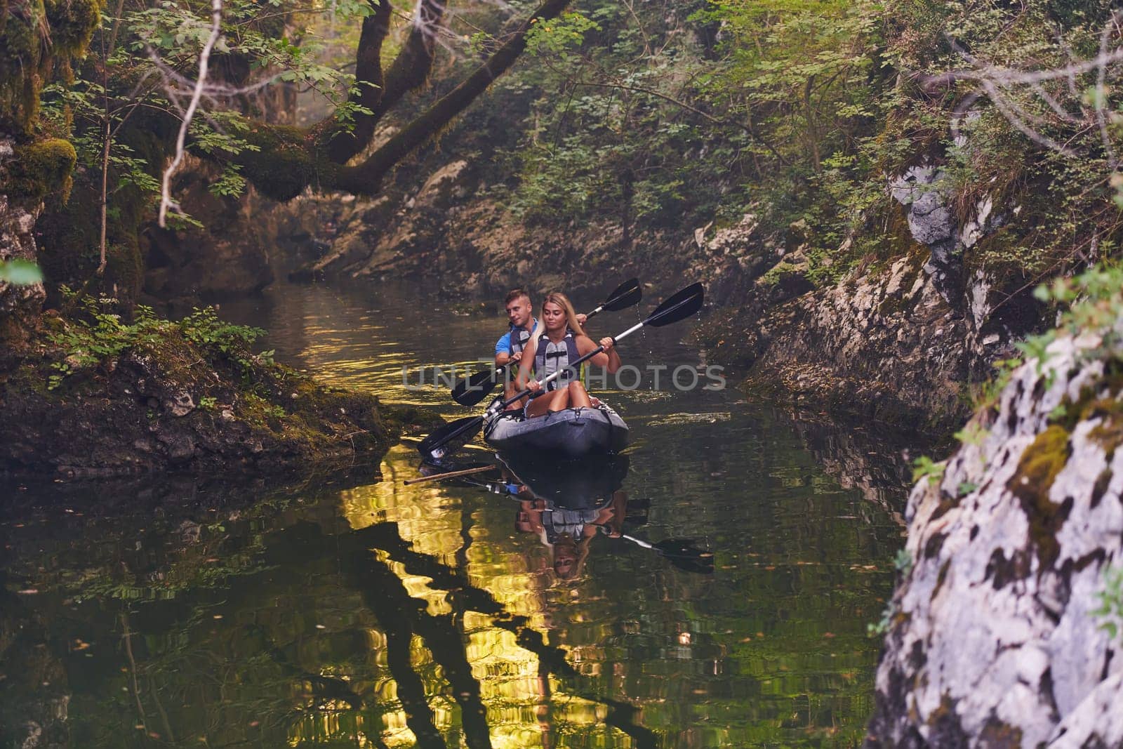 A young couple enjoying an idyllic kayak ride in the middle of a beautiful river surrounded by forest greenery.