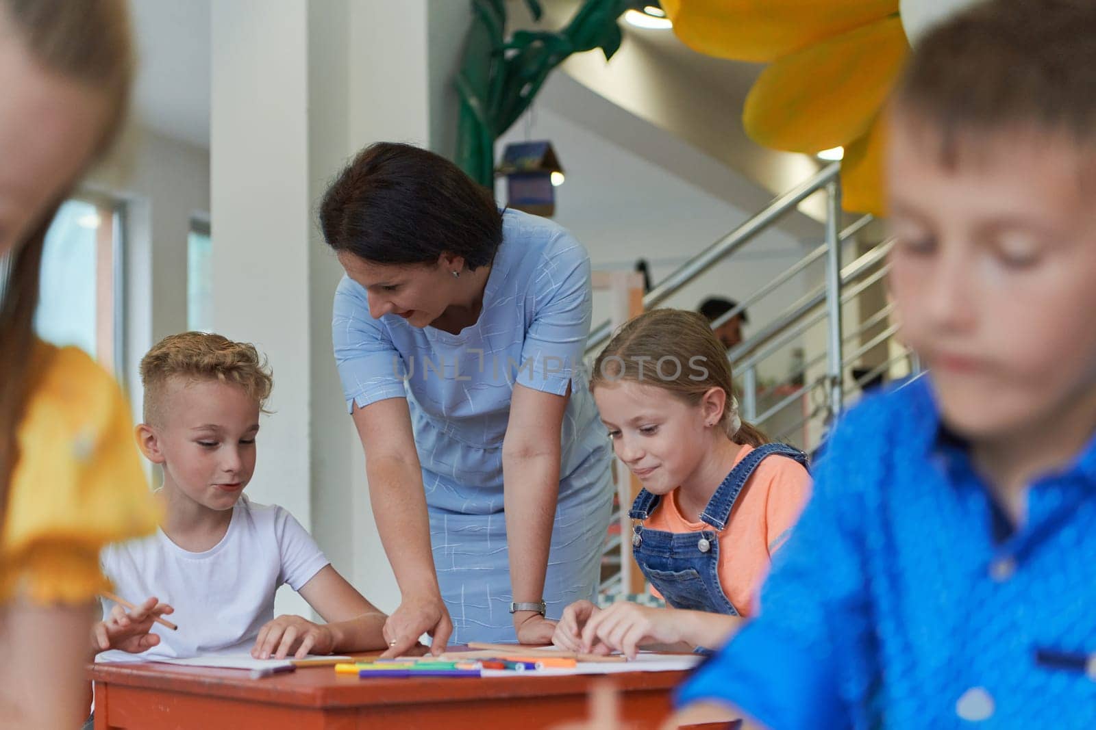 Creative kids during an art class in a daycare center or elementary school classroom drawing with female teacher