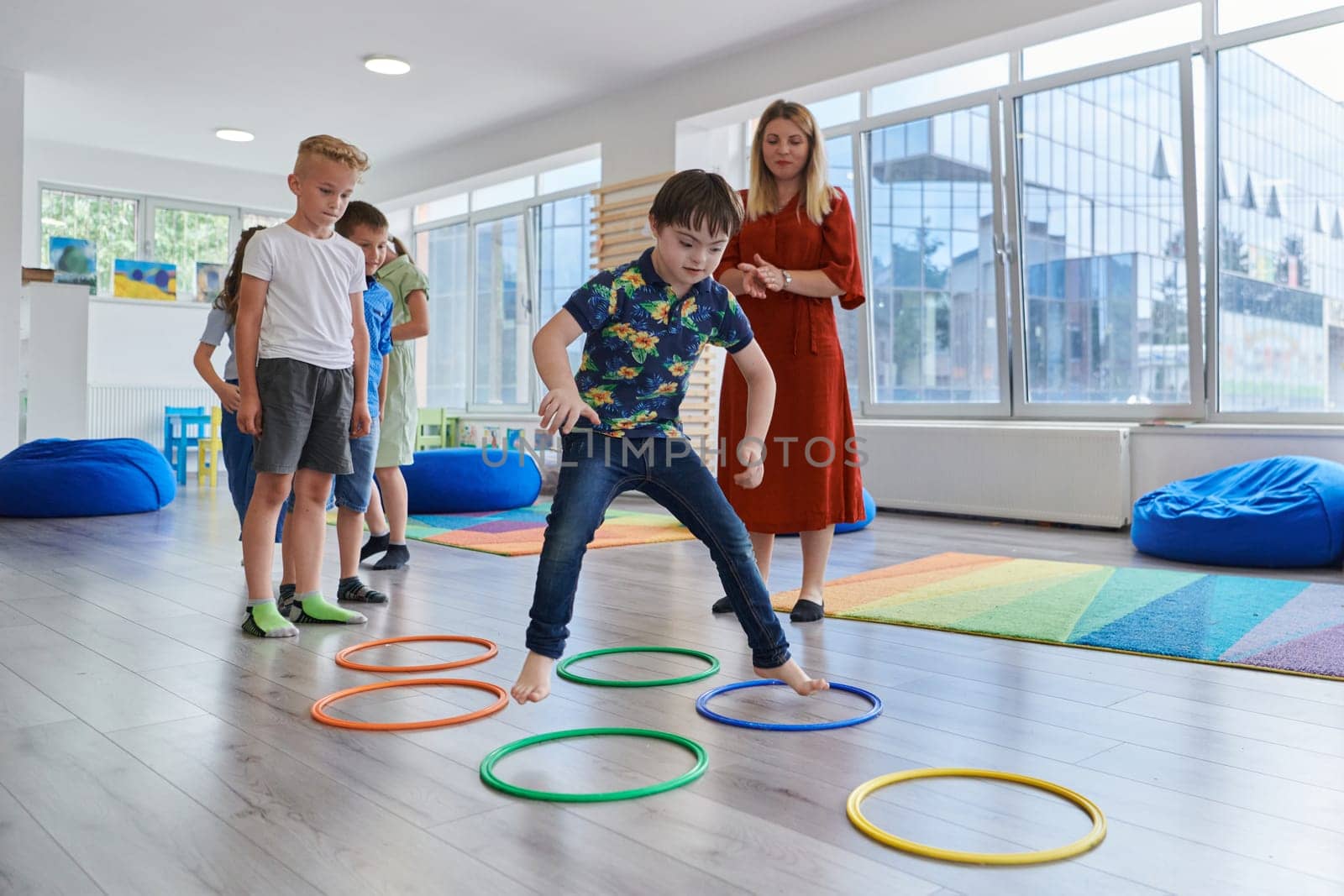 Small nursery school children with female teacher on floor indoors in classroom, doing exercise. Jumping over hula hoop circles track on the floor