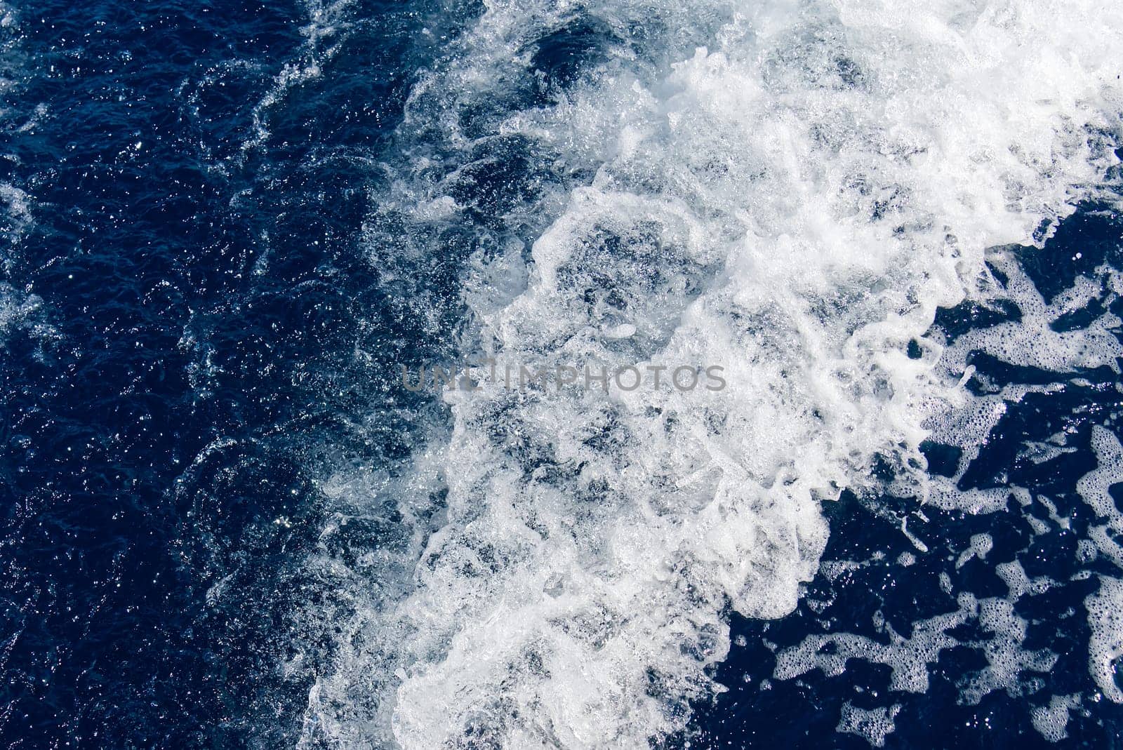 Abstract blue sea water with white waves. Blue sea texture with waves and foam. Rough deep turquoise and blue Mediterranean sea. Sea water top view.